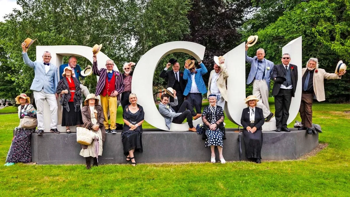 People gathered in Joycean style costumes standing in front of a large DCU sign 