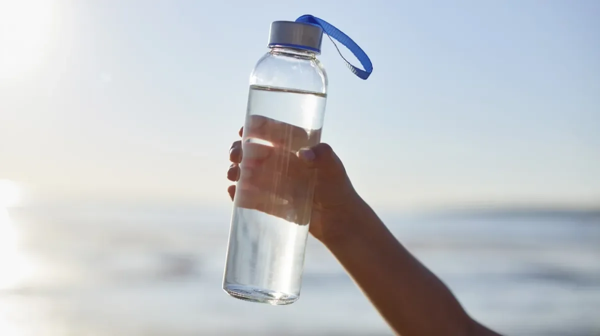 Boy holding bottle of water in air with sea in the background