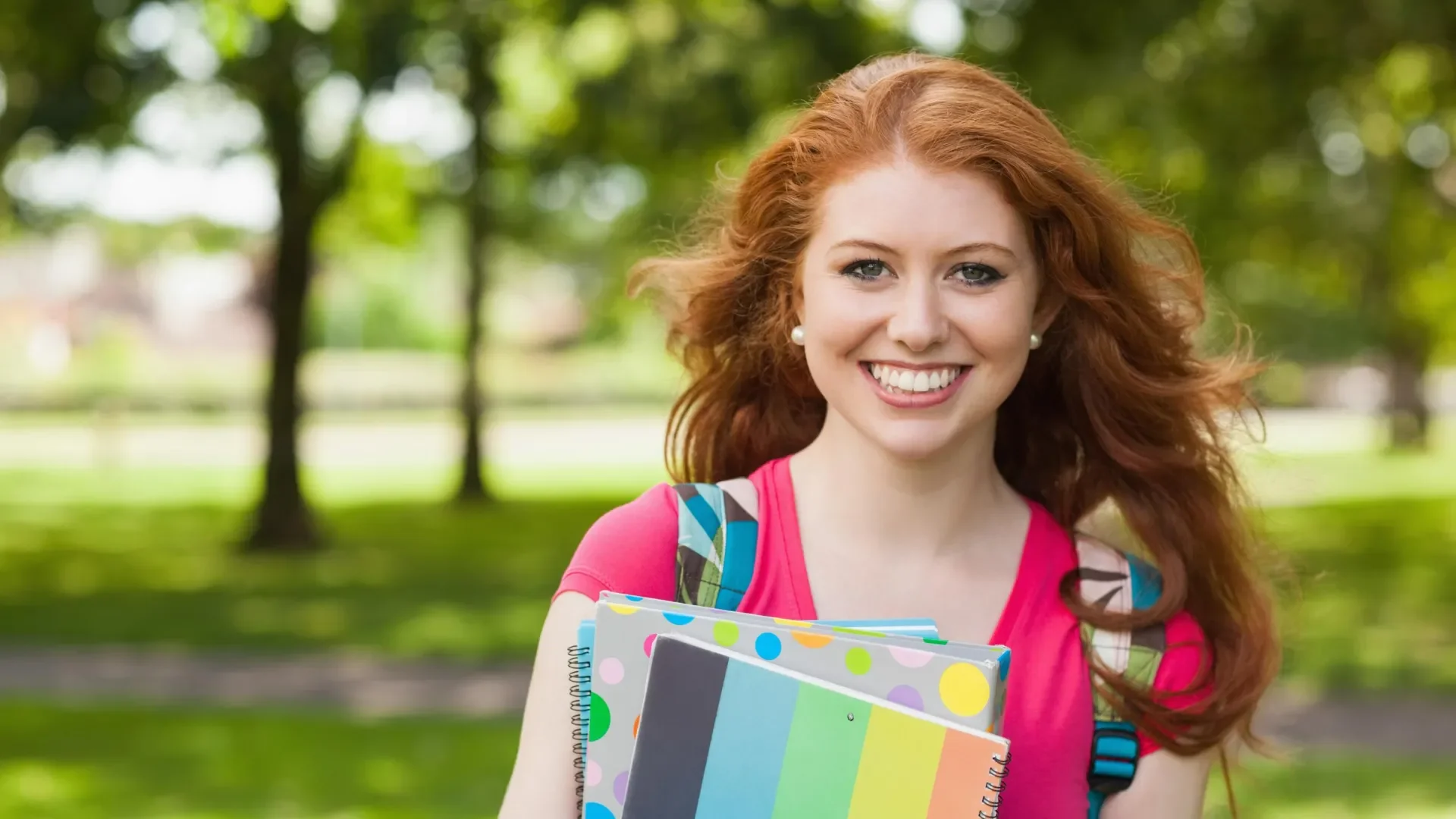 Female student with a backpack and holding books in the park 