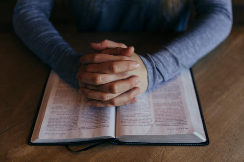 Hands classed in prayer across large Bible