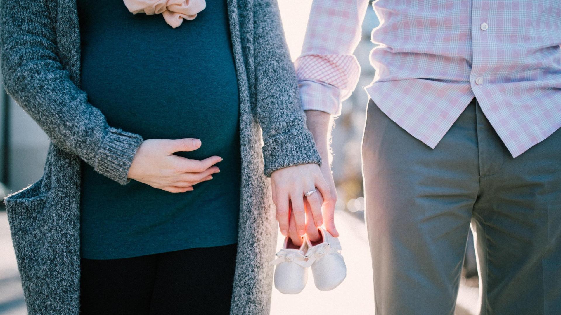 Man and Pregnant Woman holding hands with 2 baby shoes in their hands
