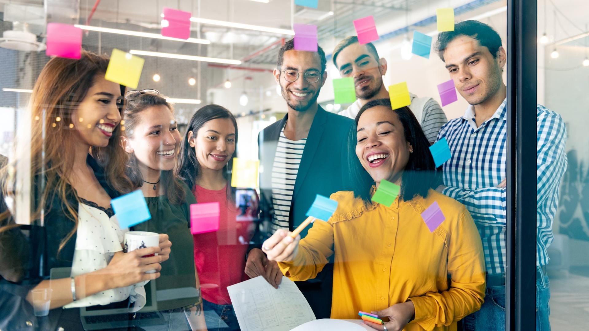 A group of colleagues brainstorming using post-it notes on a glass wall.