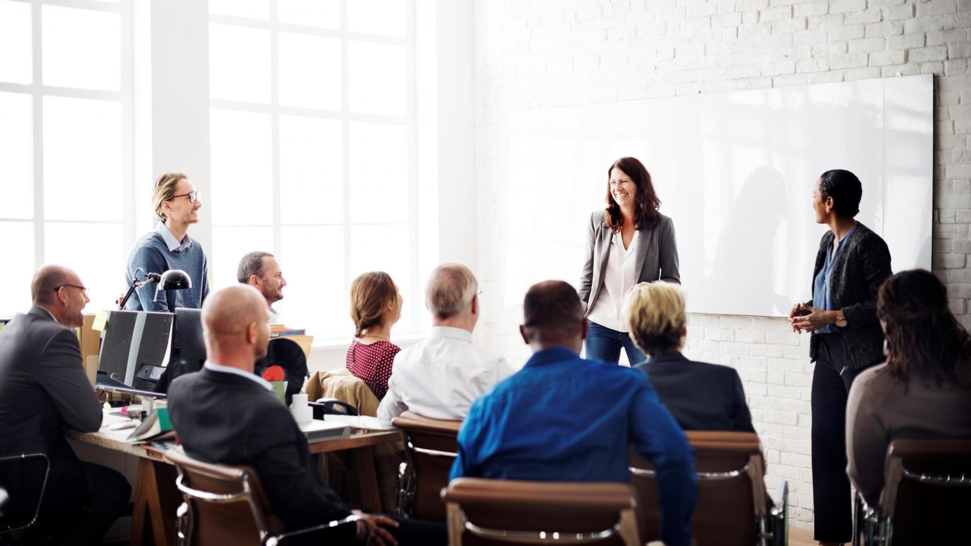 A woman standing at the top of the room speaking to a gathering of people.