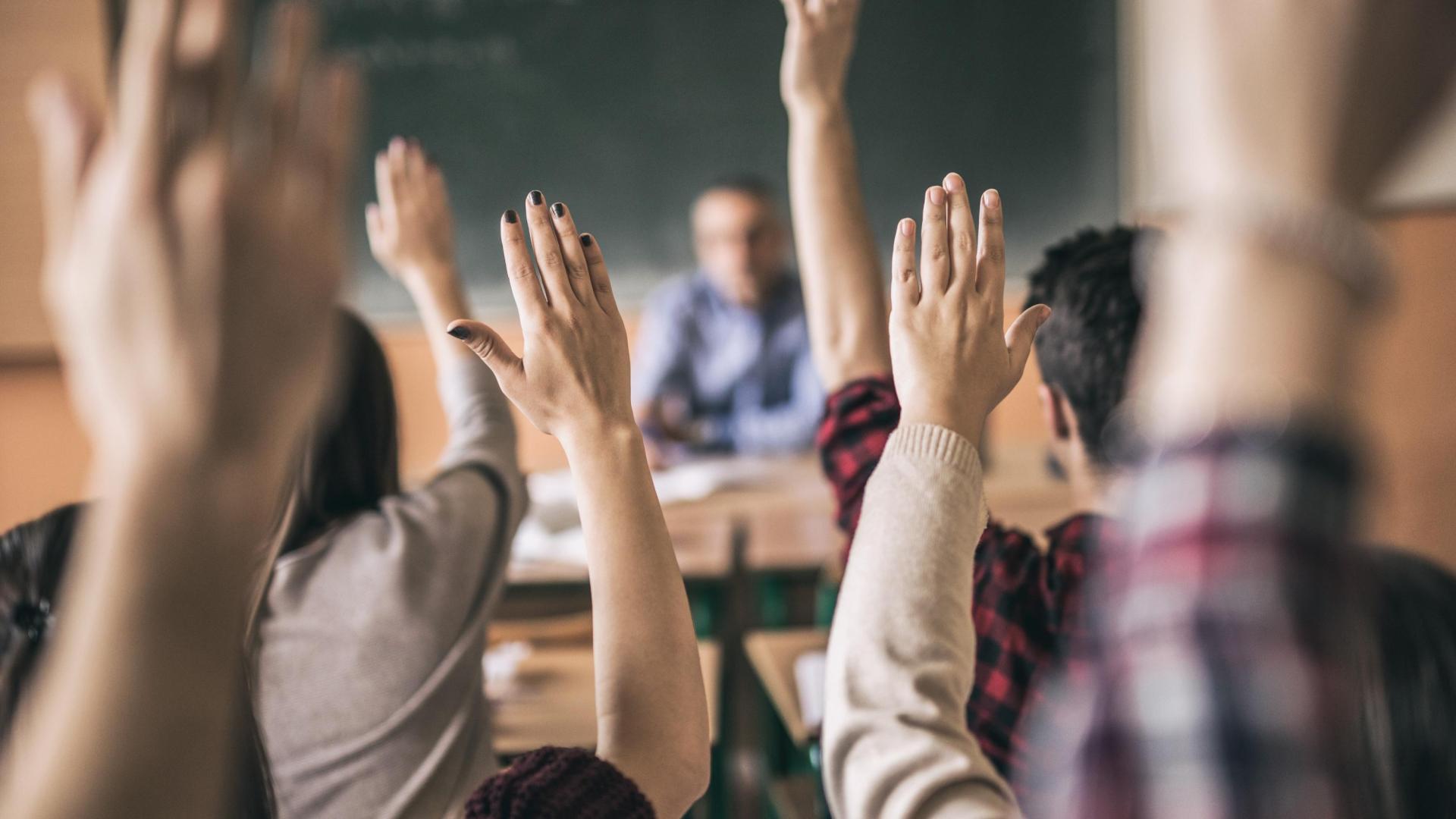 A group of people facing away from the camera with raised hands looking towards a male teacher 