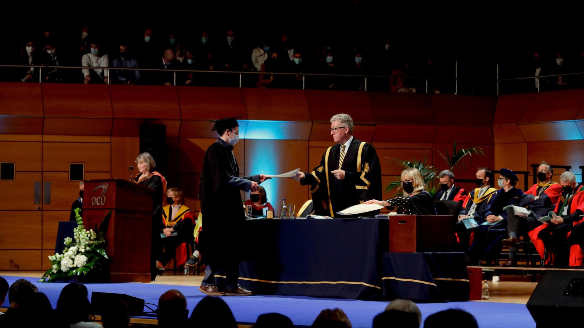 Graduate walks across the stage in O'Mahony Hall in the Helix