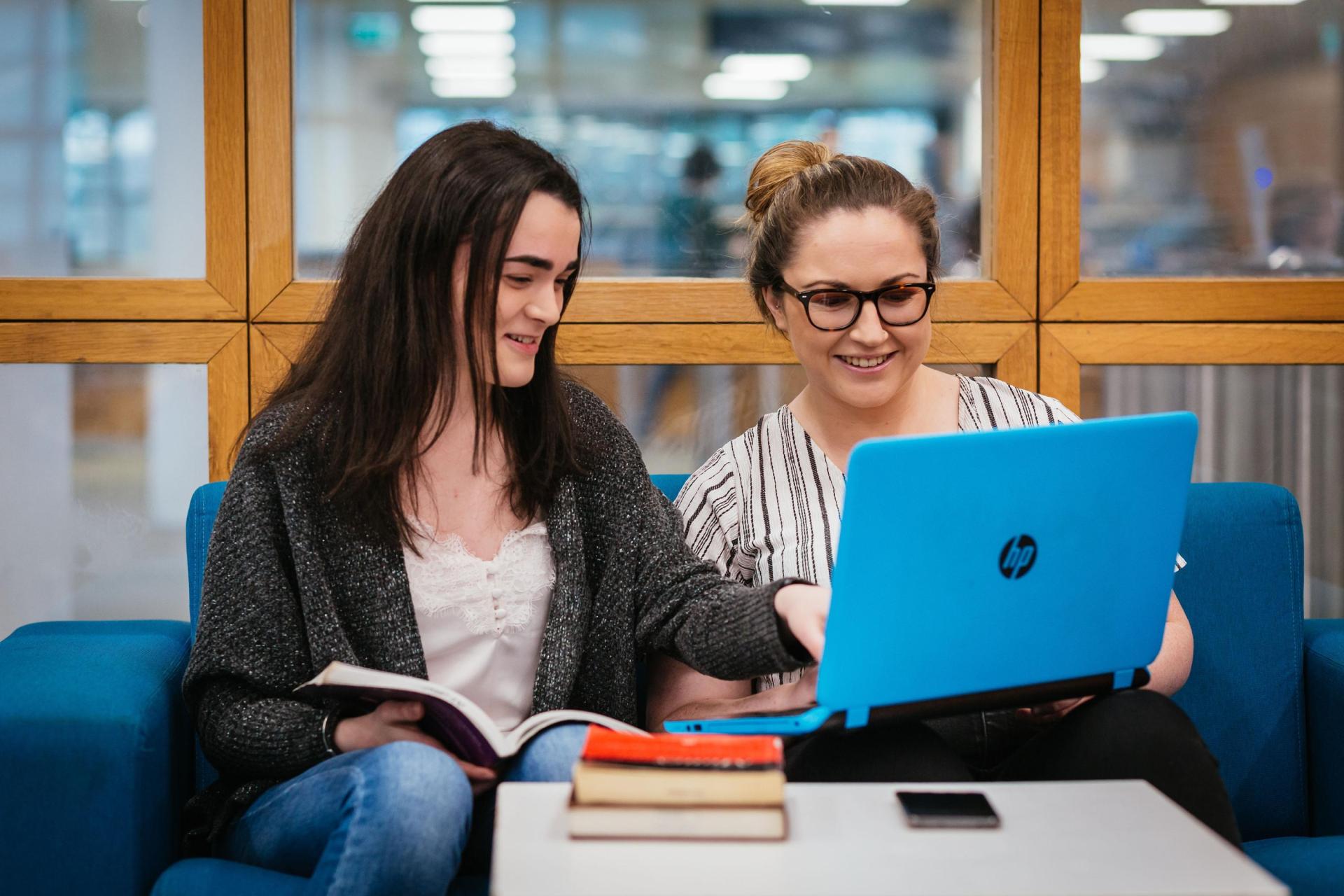 Two students sitting on a sofa reading from a laptop.