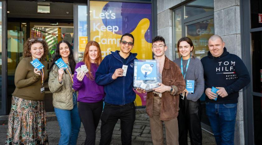 7 people from DCU holding a condom machine you can find in certain locations on campus