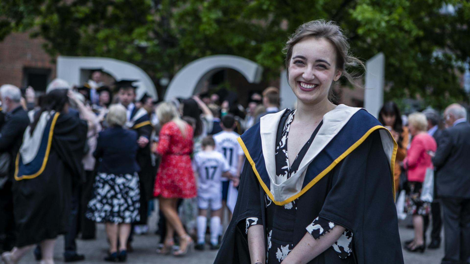 A woman poses for the camera, smiling widely, in a graduation cap and gown.