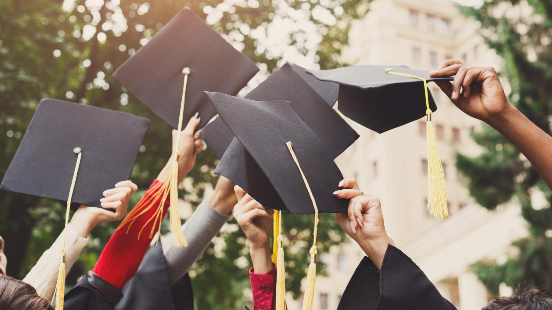 Image of group ands holding square academic caps aloft