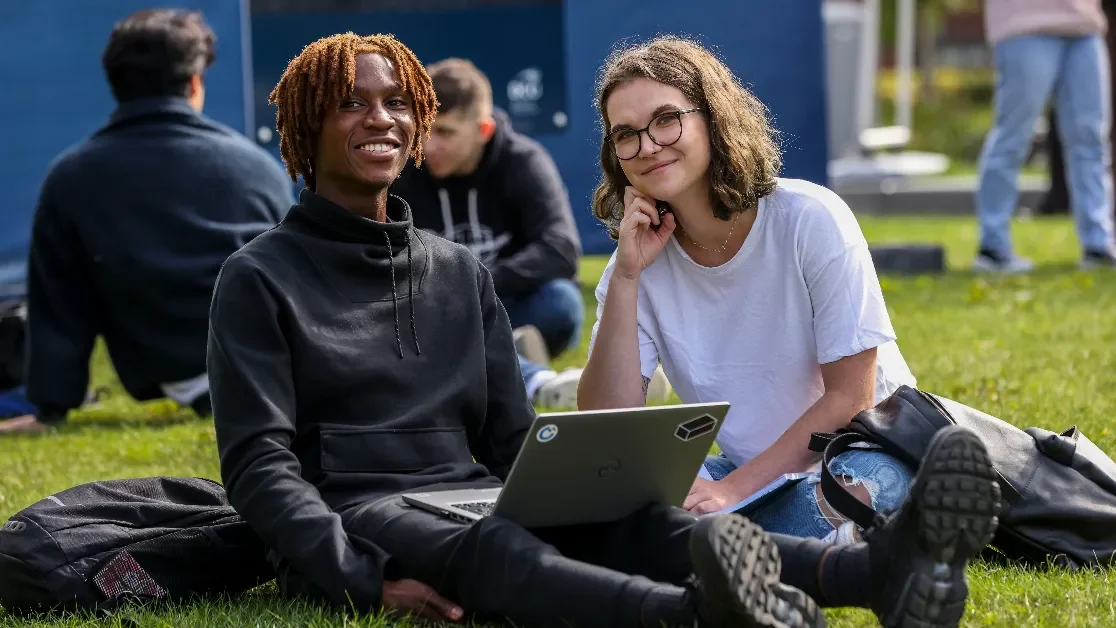 Two students sit on the grass