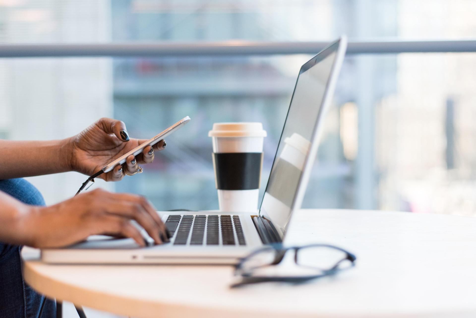 An individual holding a phone while using a laptop