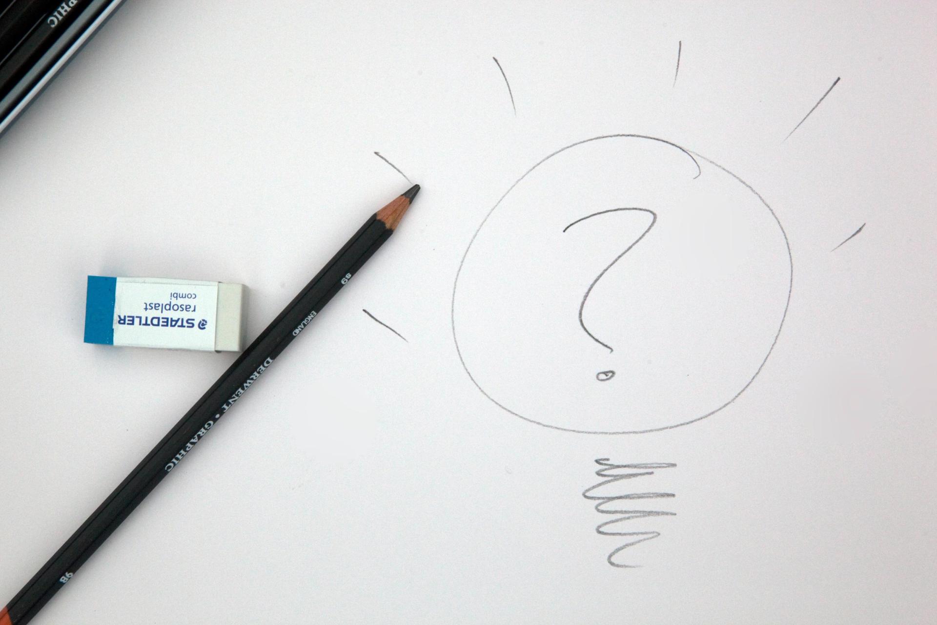 Lightbulb with question mark in the middle drawn on white paper with a pencil and rubber beside it