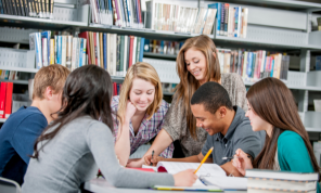 Shows six students gathered around a table in a library