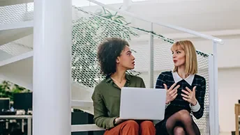 2 women talking while one holds a laptop