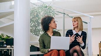 2 women talking while one holds a laptop