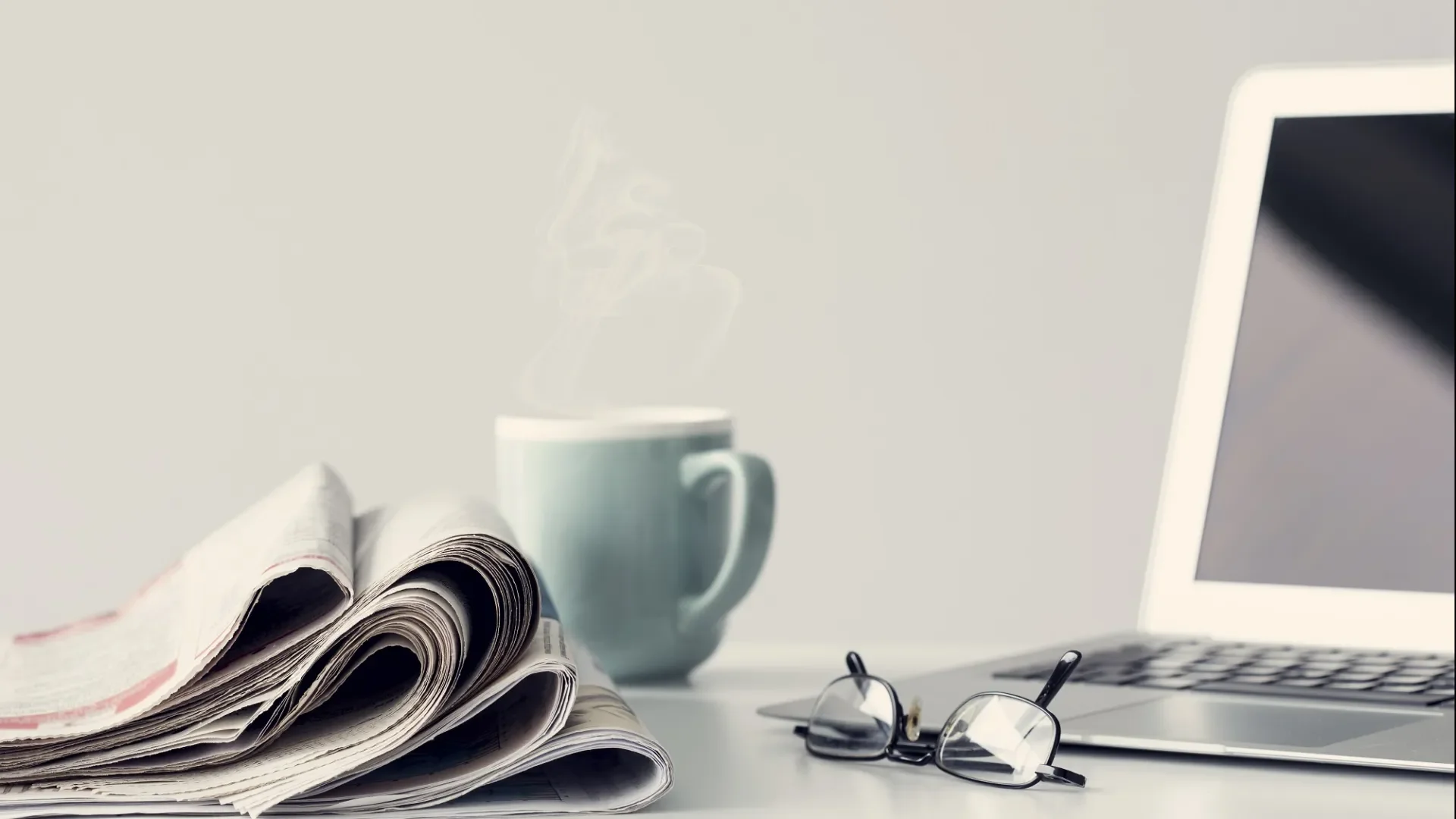 Coffee cup and newspapers beside laptop