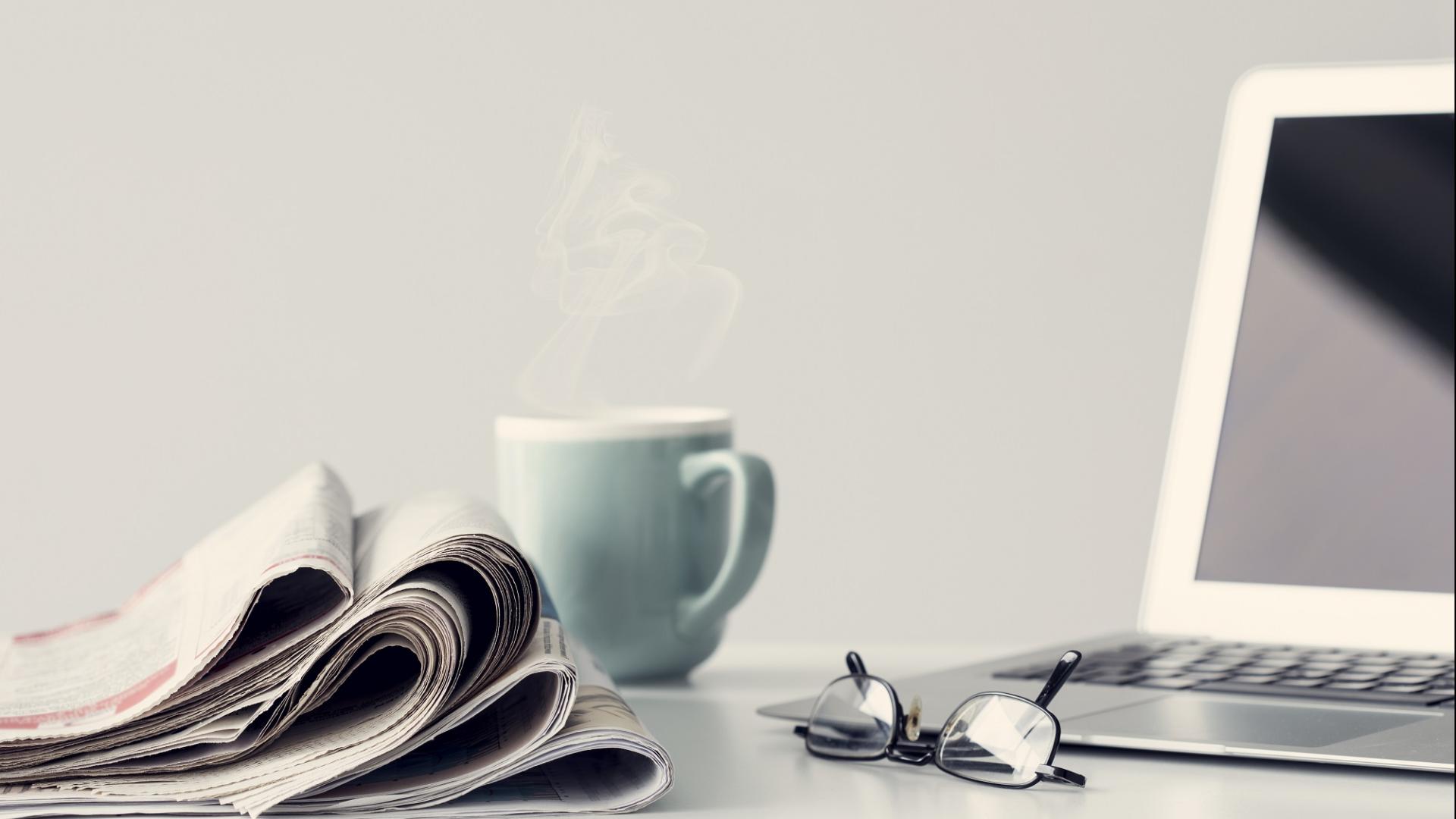 Coffee cup and newspapers beside laptop