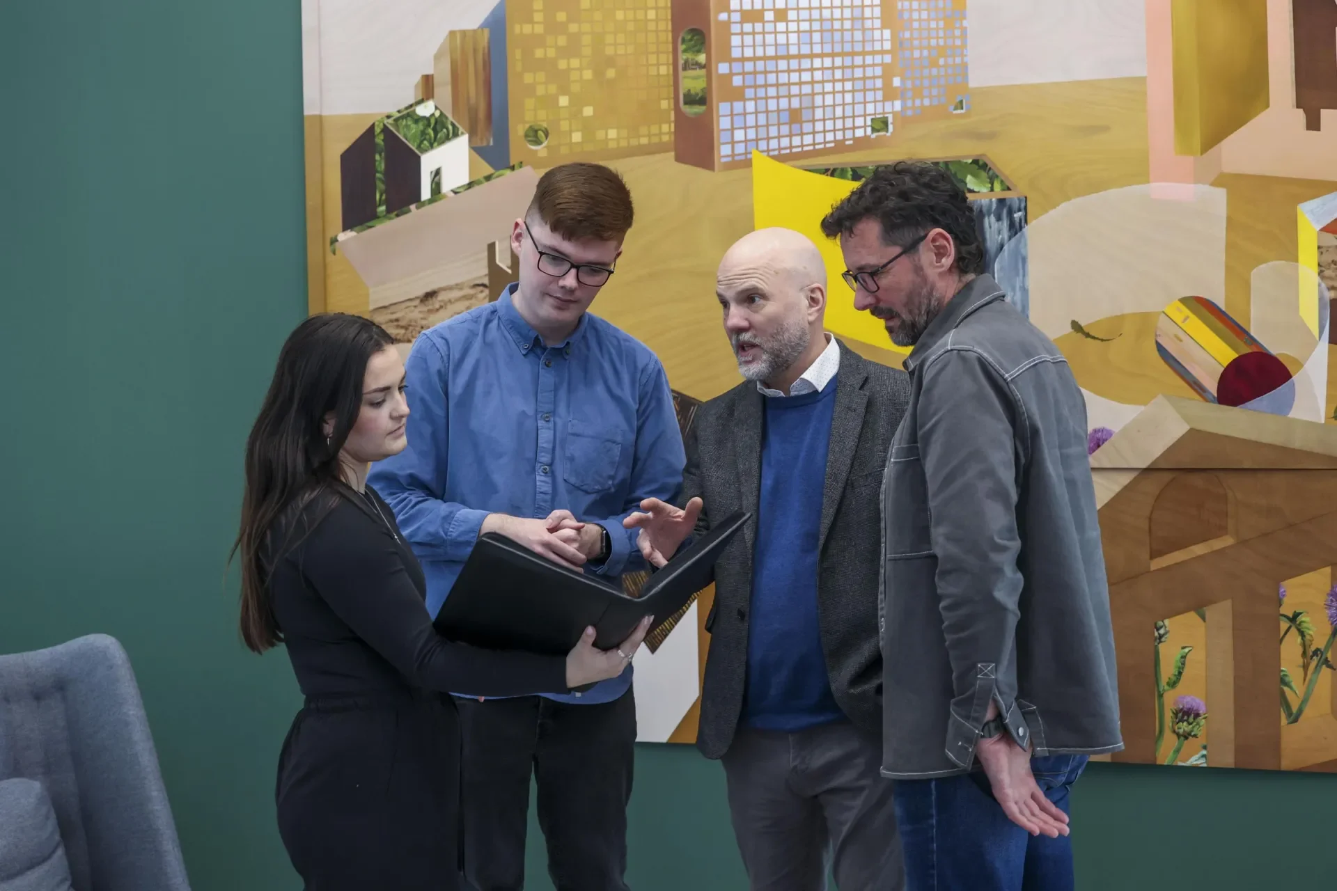 four staff members standing chatting while reviewing notes