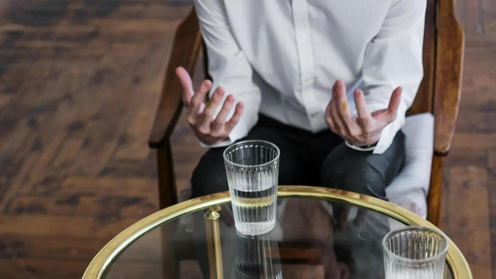 Man at glass table, head unseen, talking to a counsellor,  using his hands to express himself,
