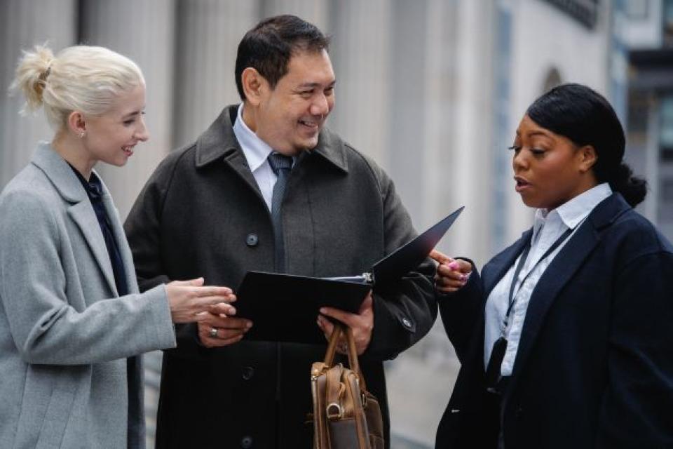 Three colleagues standing reviewing a binder