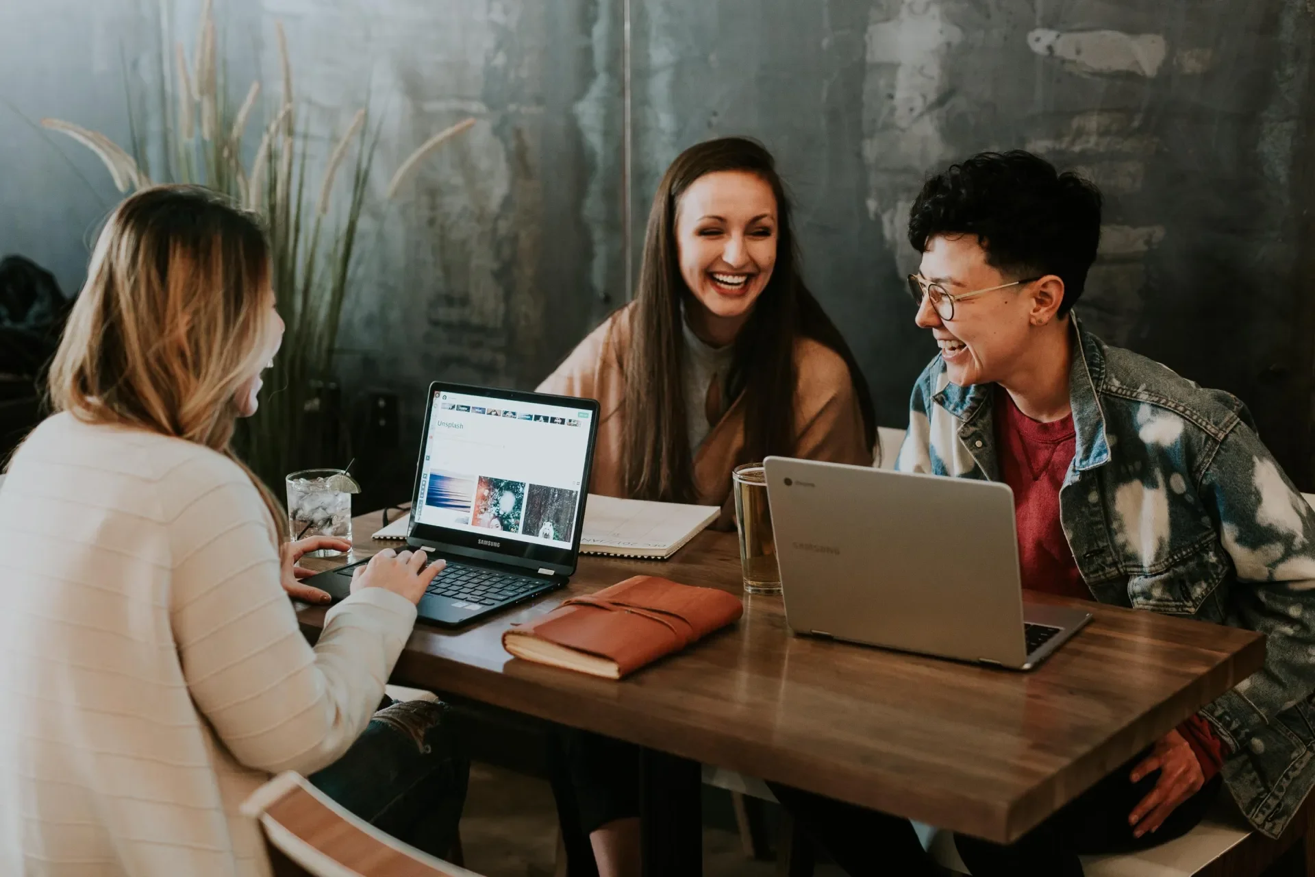 three women at table with laptops chatting and laughing