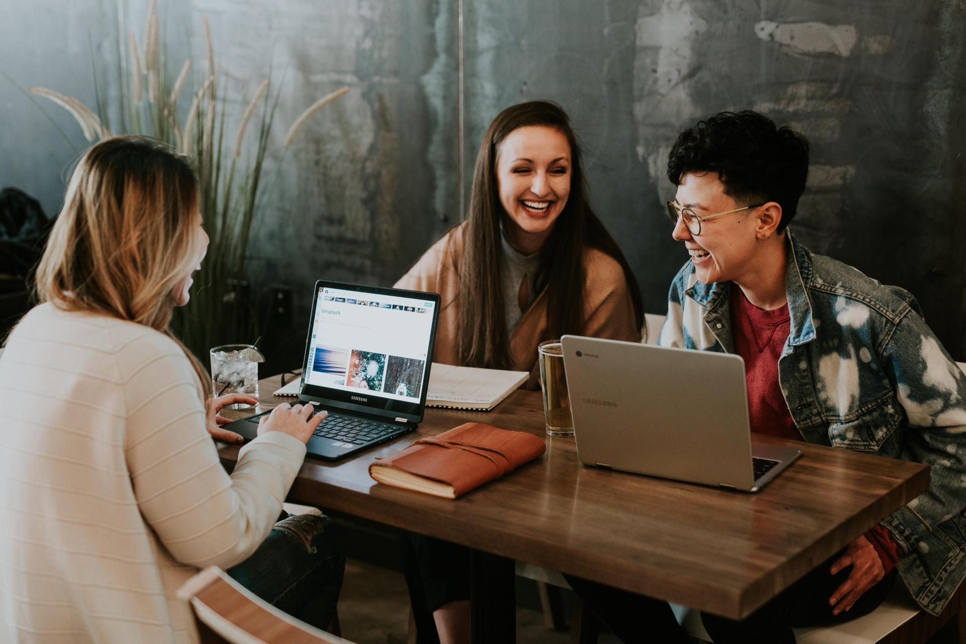 three women at table with laptops chatting and laughing