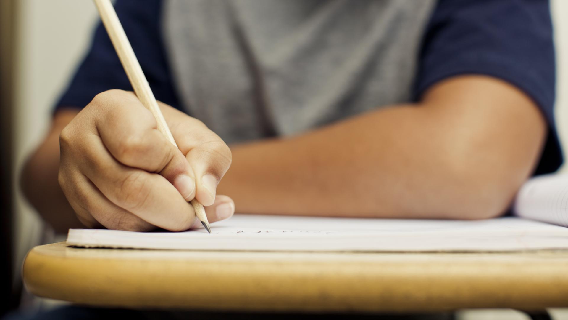 Shows close up of child using pencil to write in exercise book