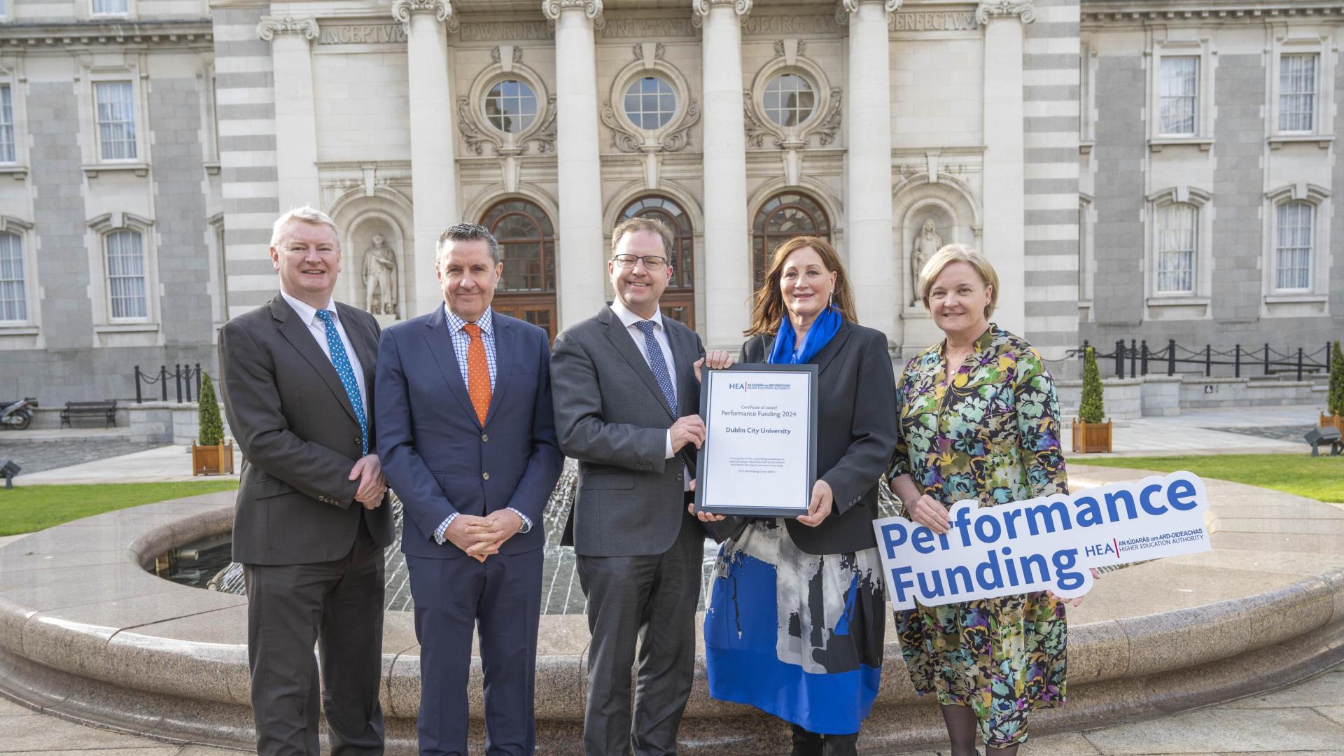 Five educators holding an award in front of a very nice building