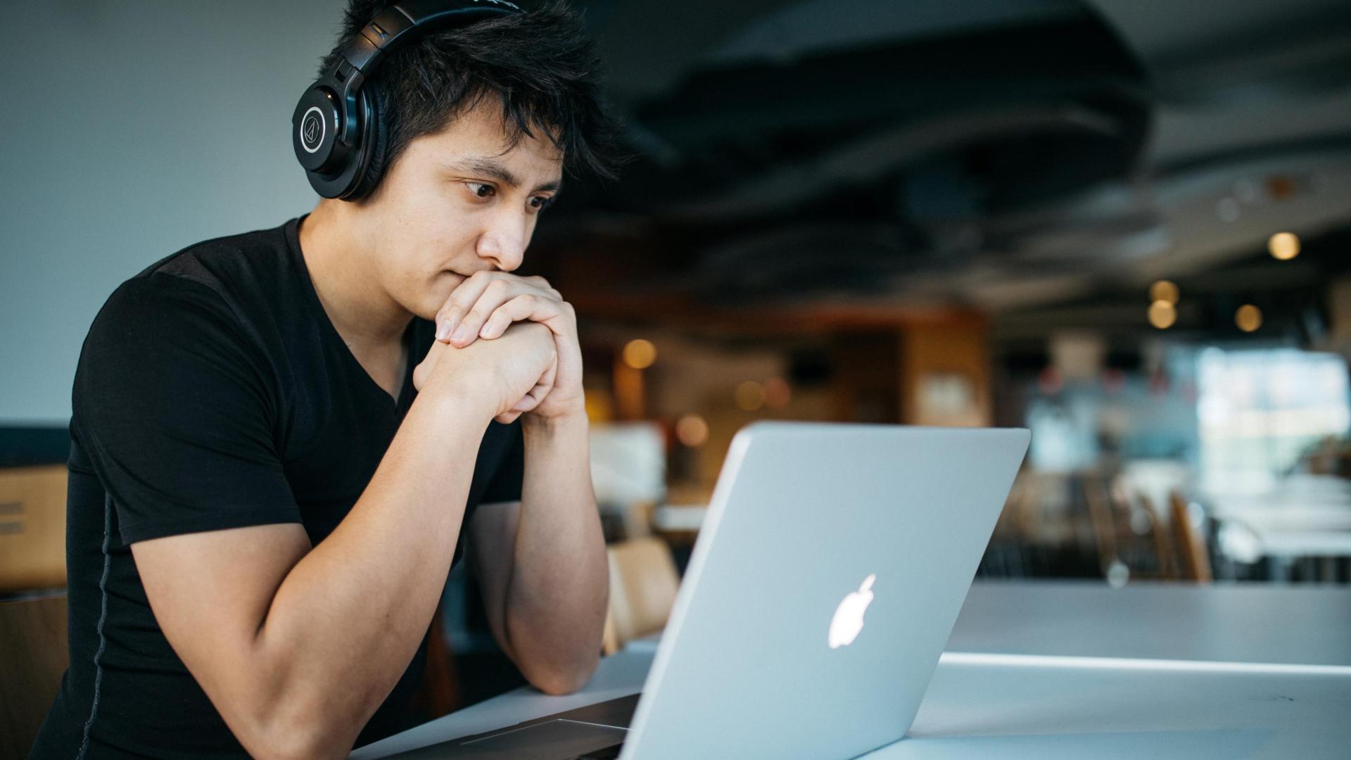 A man sitting in front of a laptop with earphones on.