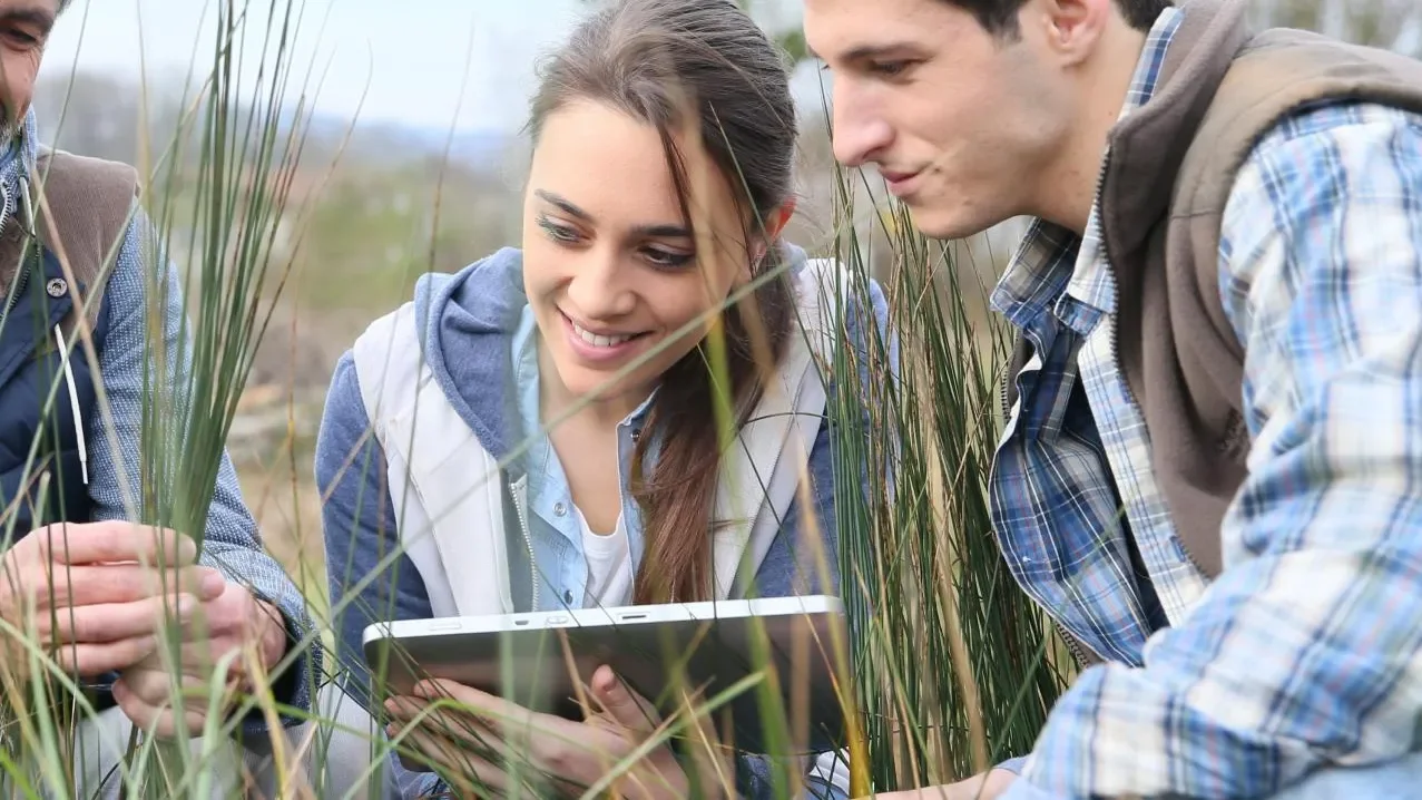 Three students on the grass collaborating on an iPad