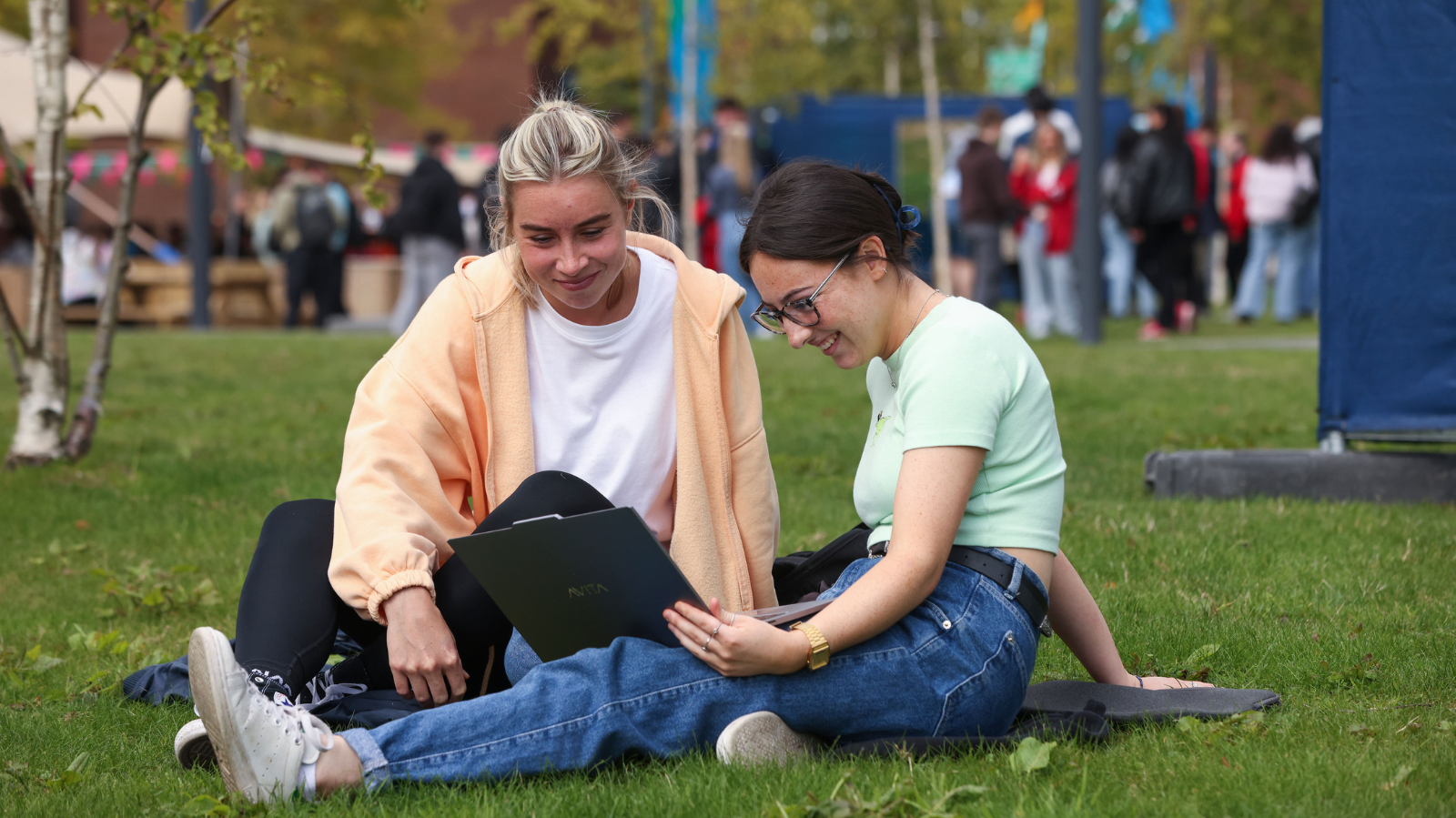 students stiing on the grass on Glasnevin campus, both looking at a laptop 