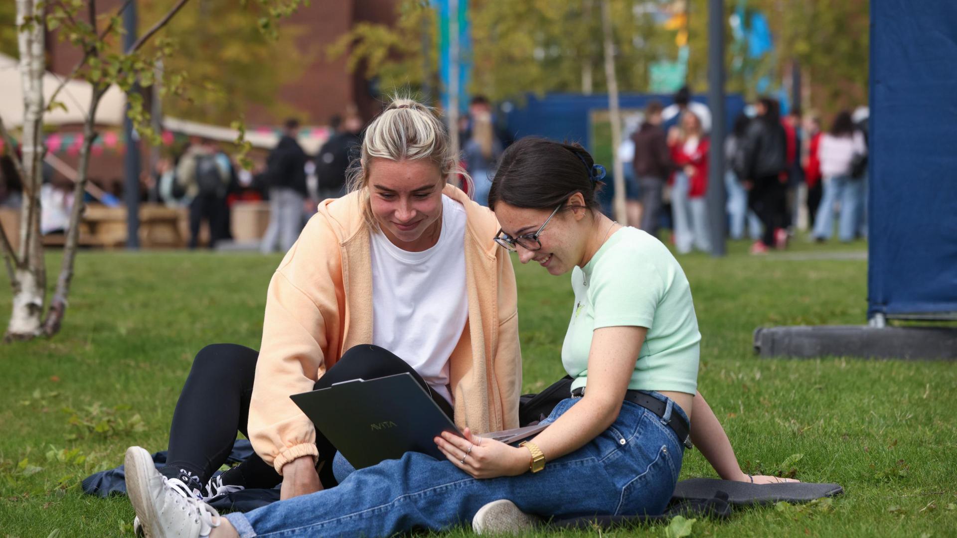 2 students sitting outside the U building on Glasnevin campus
