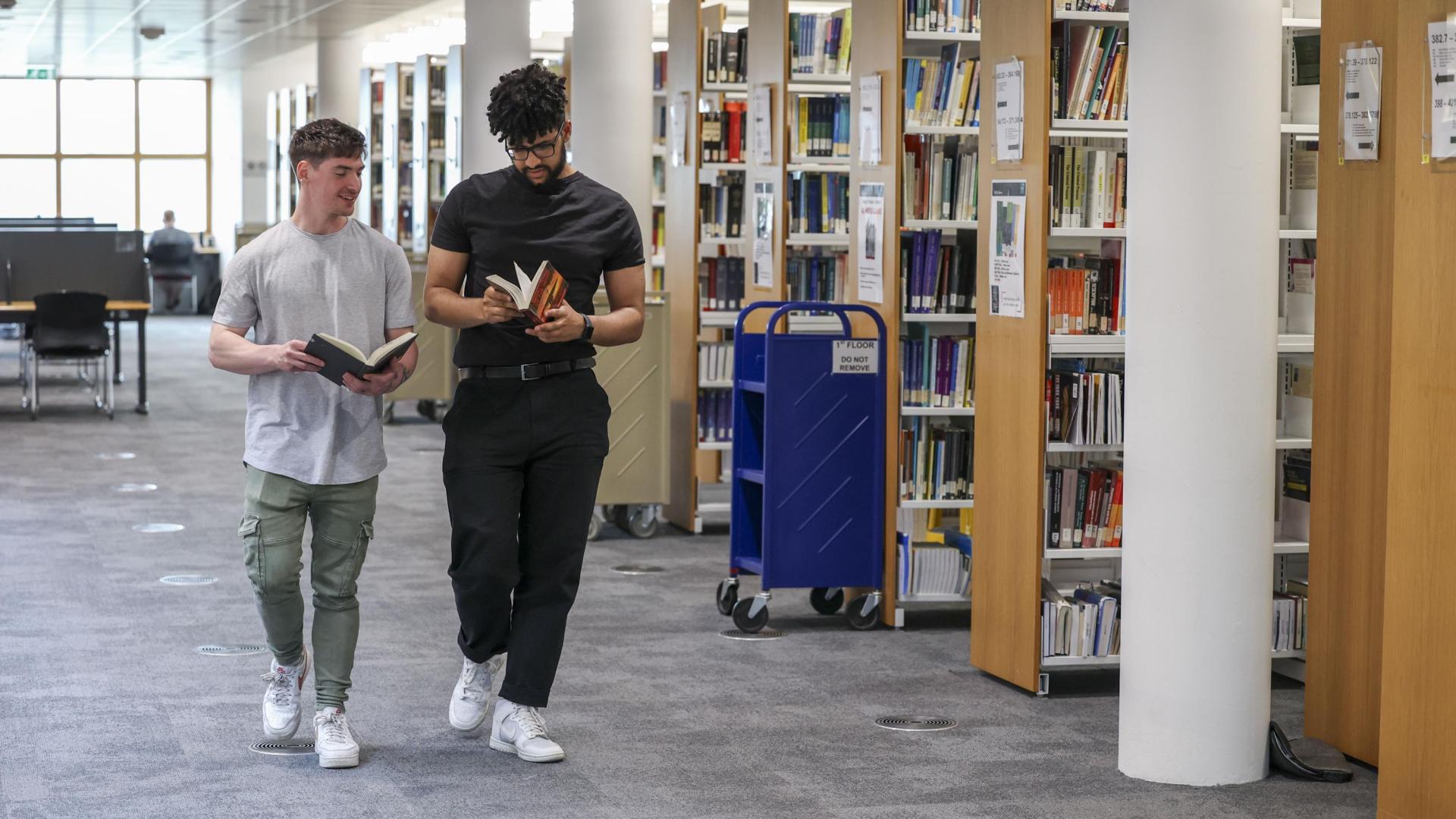 2 students walking and chatting near the book shleves on the first floor of O' Reilly library