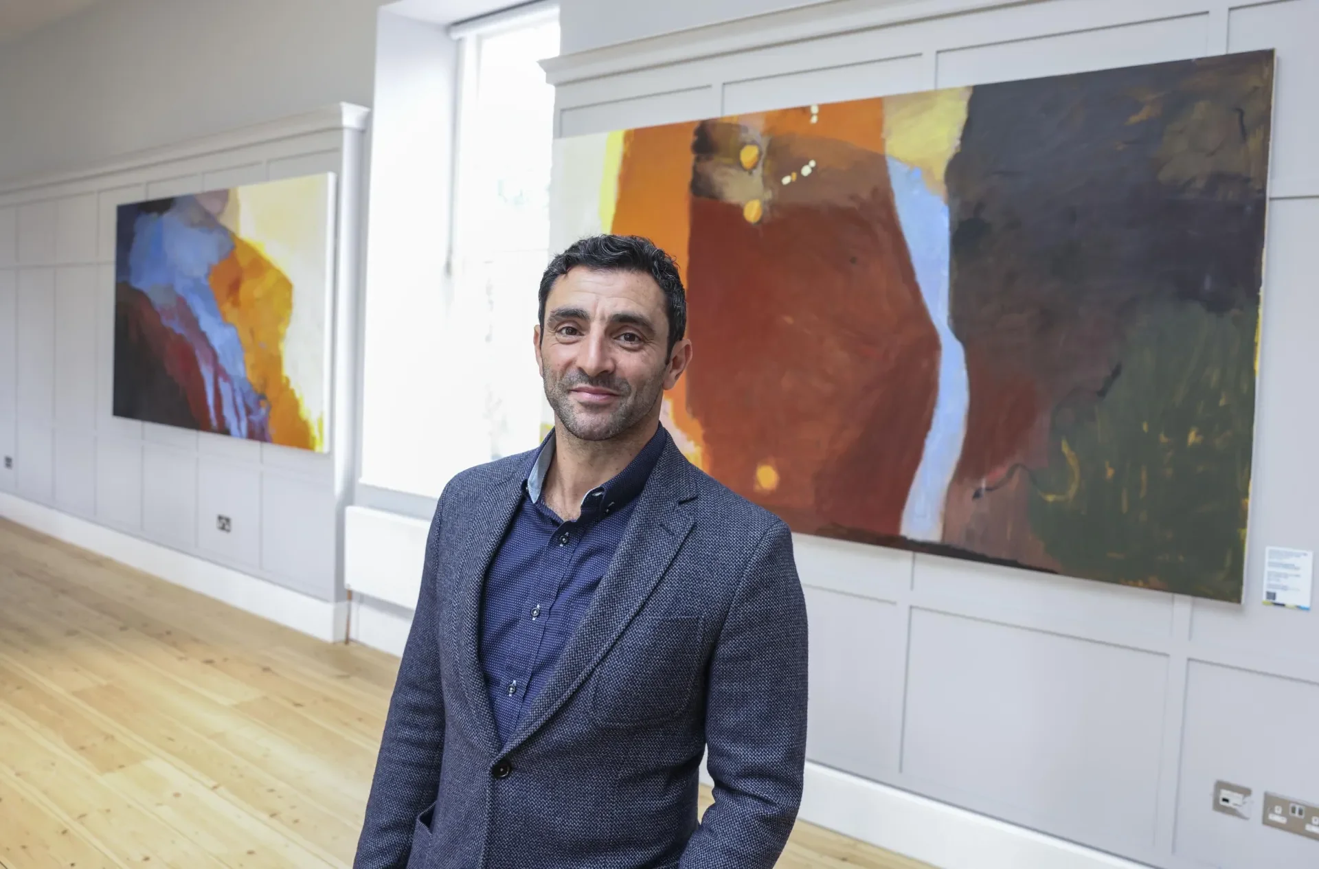 Artist, Richard Hearns, a man in a blue blazer stands in front of his artwork NEXUS - a colorful abstract diptych piece 