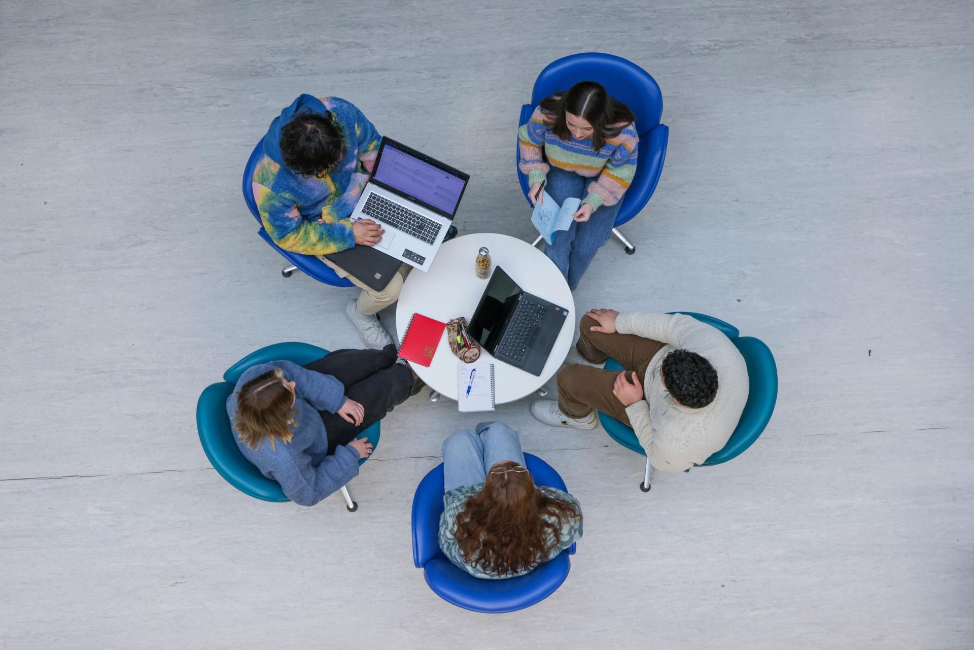 5 people sitting around a small table having a meetingg