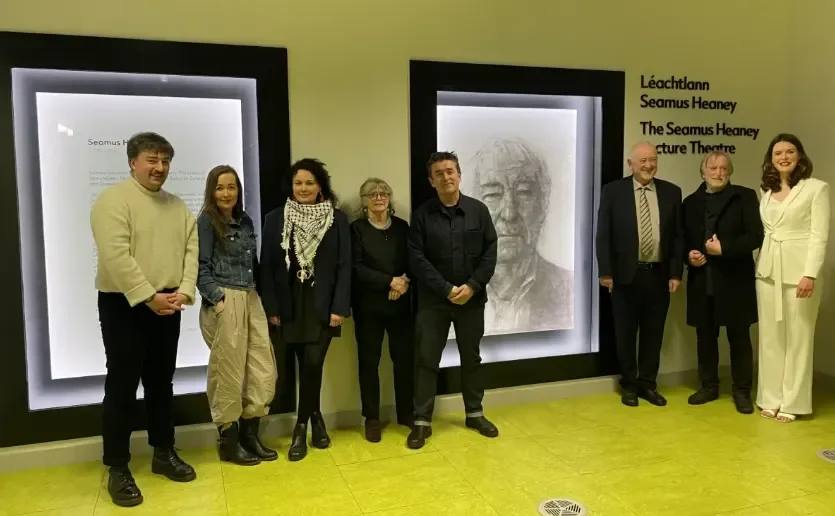 8 people stand in front of a portrait of Seamus Heaney
