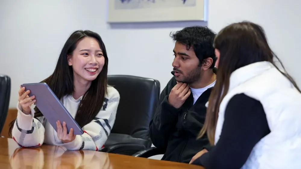 Students talking and looking at a tablet sitting around a table